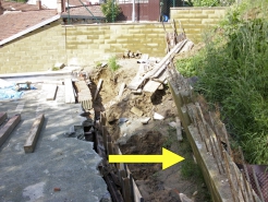Obr. 12: Zničená opěrná zídka (šipka) – vlevo střecha garáží; viz i obr. 16